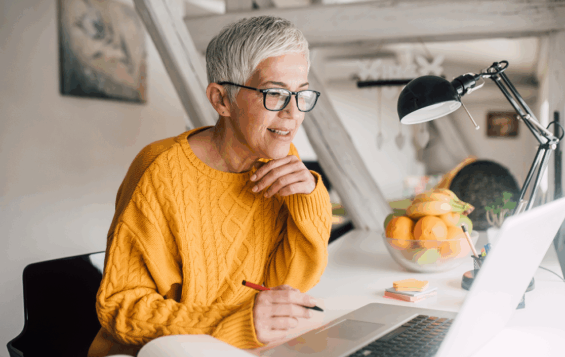 A woman at her desk looking at her laptop writing notes