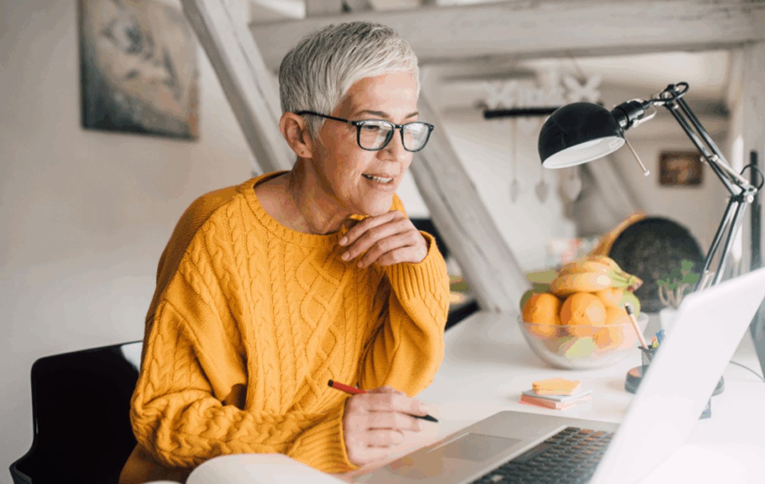 A woman at her desk looking at her laptop writing notes
