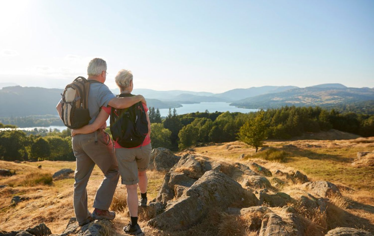 A couple stood atop a hill looking over views of a lake, trees and hills