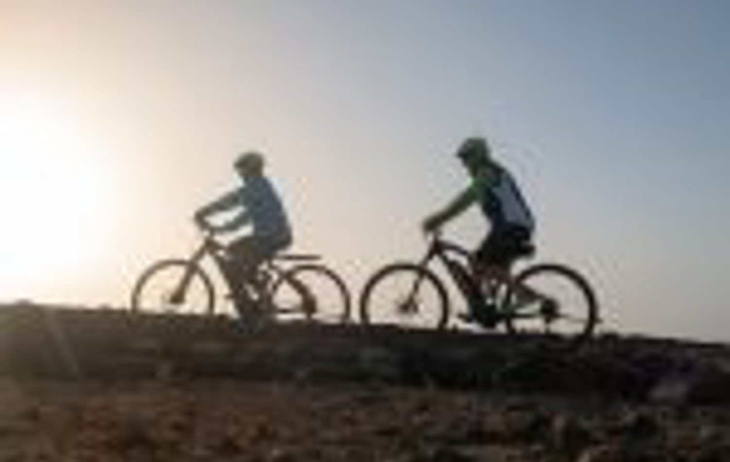 Two people riding bicycles in the sunset