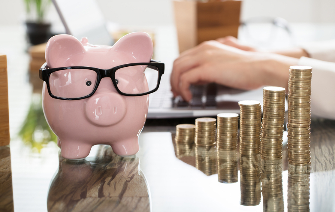 A piggy bank wearing glasses beside stacks of coins that gradually increase
