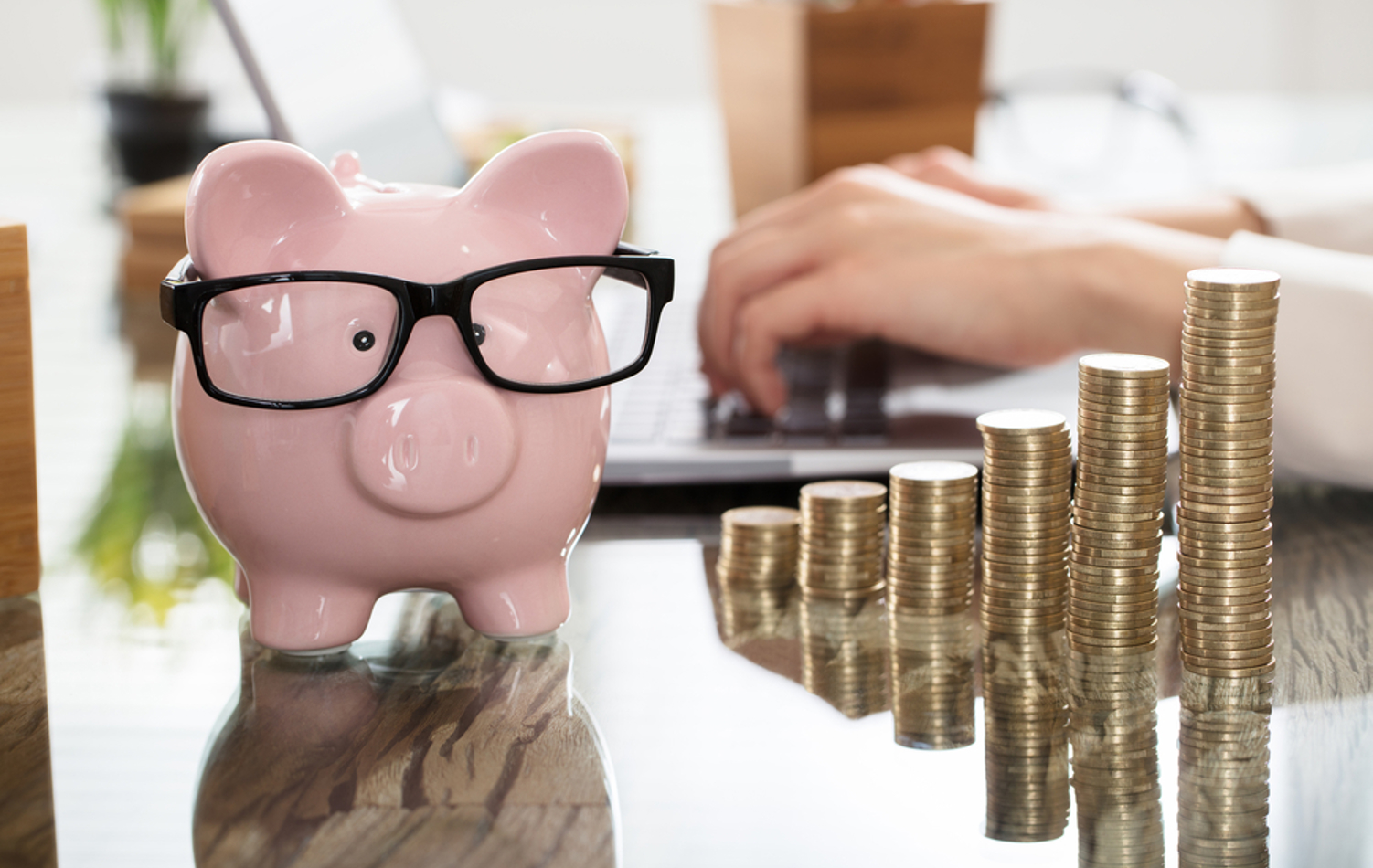 A piggy bank wearing glasses beside stacks of coins that gradually increase